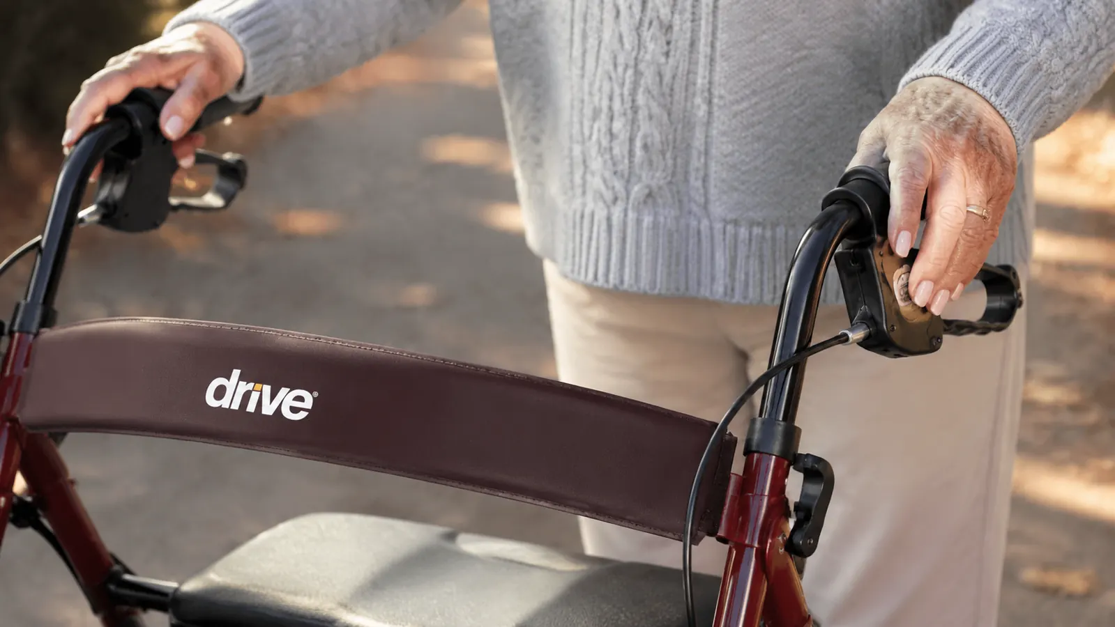 Close-up of hands gripping rollator walker handles with padded grips, outdoors on a paved path