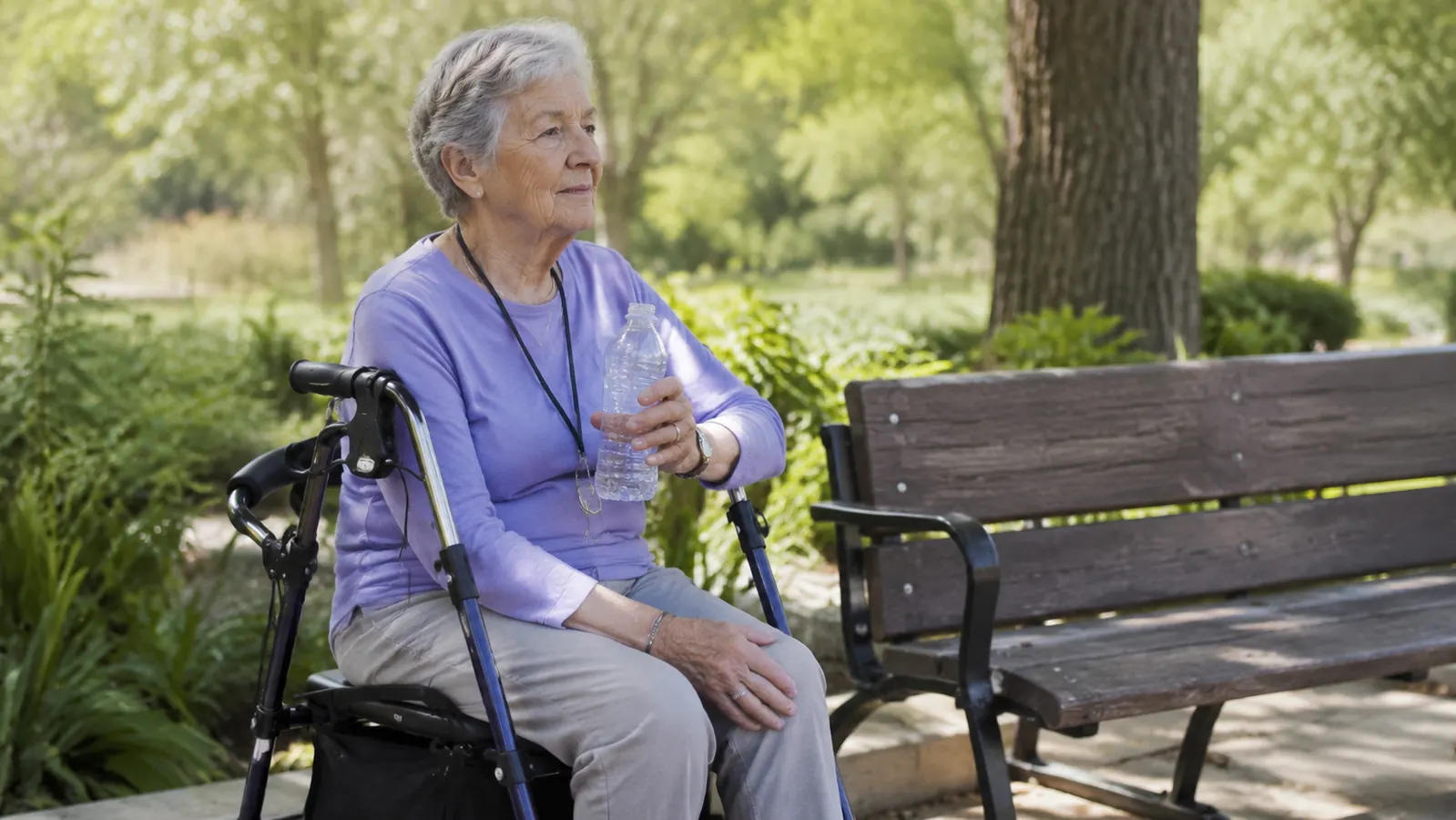 Senior woman sitting on rollator walker seat at a park, resting comfortably