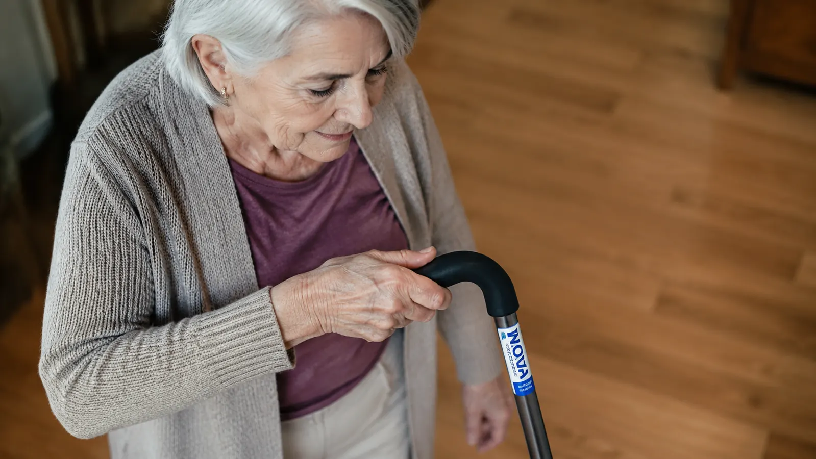 Close-up of the offset handle grip and wrist angle while a hand holds the NOVA cane on a wood floor